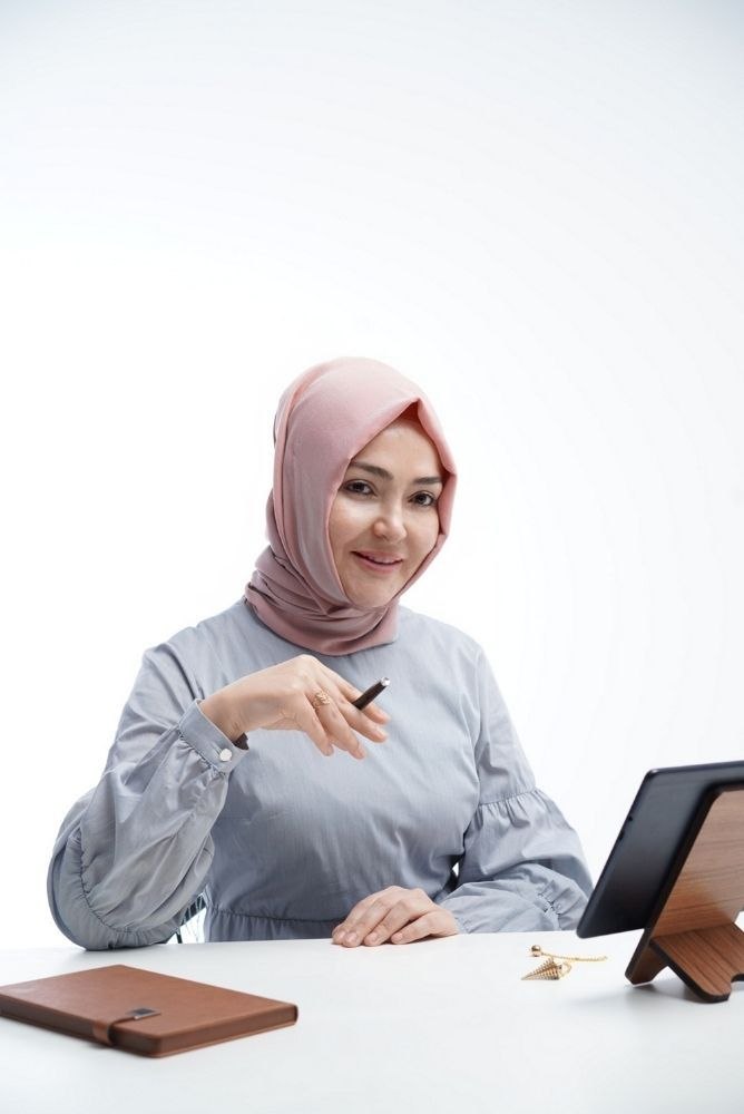 Kerime Melike Kaan, elinde kalemle masada oturuyor